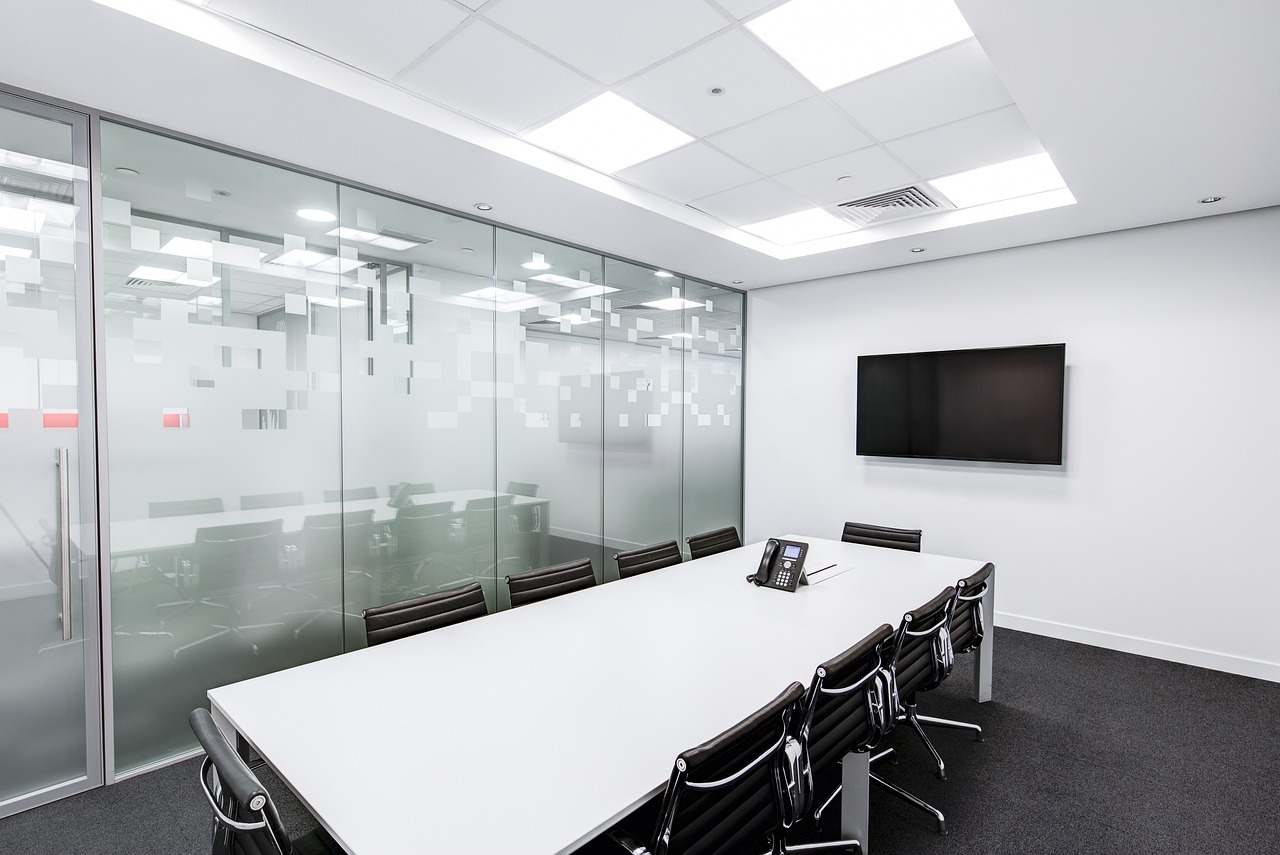 An empty boardroom with a long table and a wall screen